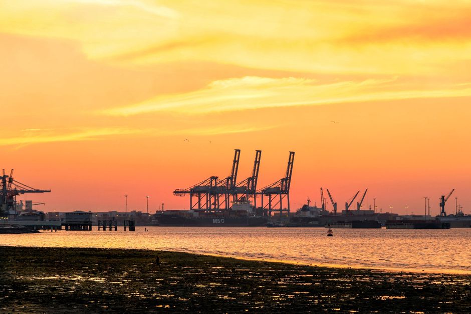 Navios e contêineres em um porto ao pôr do sol, símbolo da vitalidade do comércio exterior.